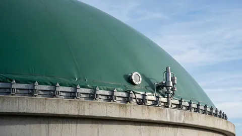 Zielony dach dwumembranowy na betonowym fermentorze: napięta membrana, stalowy pierścień mocujący i zawór bezpieczeństwa na tle nieba.