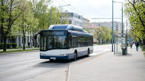 Niskopodłogowy autobus miejski na CNG z zabudową butli na dachu na przystanku w zielonej alei polskiego miasta.