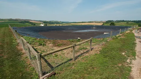 Laguna gnojowicowa przykryta czarną folią na farmie mlecznej Pennwood w Pensylwanii, otoczona drewnianym płotem.