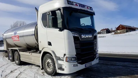 Ciężarówka z polerowaną cysterną do mleka i serwatki na zaśnieżonej drodze w górach Norwegii, w świetle zimowego dnia.