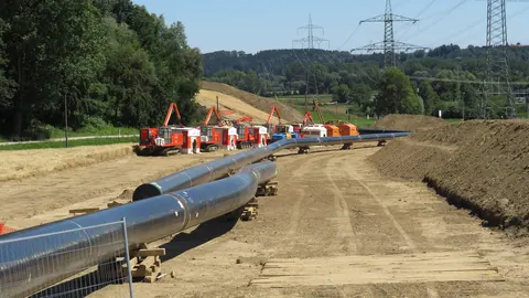Budowa gazociągu Forchheim–Finsing w Bawarii: spawany odcinek rury na podkładach wzdłuż wykopu, w tle linie wysokiego napięcia.
