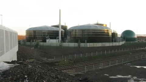 Instalacja fermentacji odpadów spożywczych Millerhill pod Edynburgiem: zbiorniki z kopułami gazowymi i komin, widziane o zmierzchu.