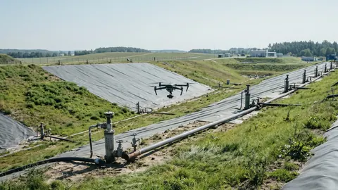 Dron z kamerą w gimbalu nisko nad kwaterą składowiska odpadów z systemem odgazowania: studnie, rury zbiorcze i geomembrana.