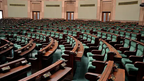 Sala posiedzeń Sejmu RP widziana z boku – amfiteatralny układ ław poselskich i kamienna okładzina ścian w ciepłym świetle.