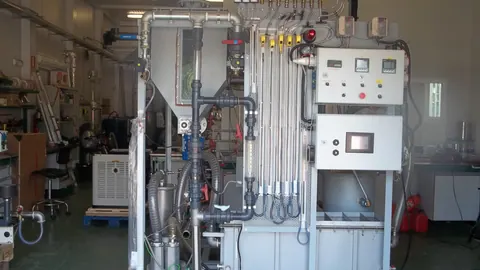Doświadczalna instalacja zgazowania biomasy w złożu fluidalnym: stalowy reaktor, cyklon i rurociągi w hali laboratoryjnej.