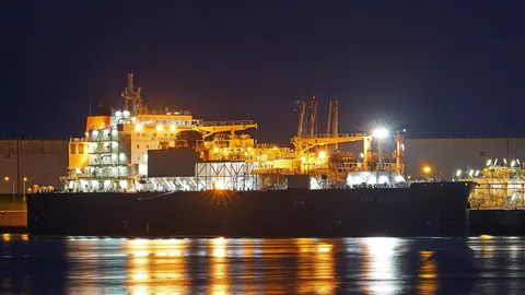 Statek do bunkrowania LNG cumujący nocą przy terminalu w porcie Rotterdam, oświetlony pokład odbija się w wodzie basenu.