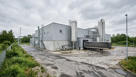 Zakład przetwarzania ubocznych produktów zwierzęcych: nowoczesna hala, stalowe silosy i kryta ciężarówka przy rampie.