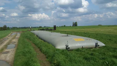 Elastyczny zbiornik workowy na gnojowicę ustawiony na skraju pola przy polnej drodze w Belgii, pod pochmurnym niebem.