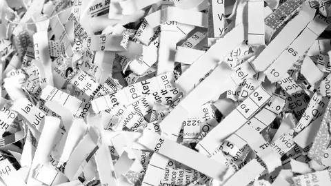 Stos pociętego w paski białego papieru biurowego z niszczarki – zadrukowane fragmenty makulatury w zbliżeniu.