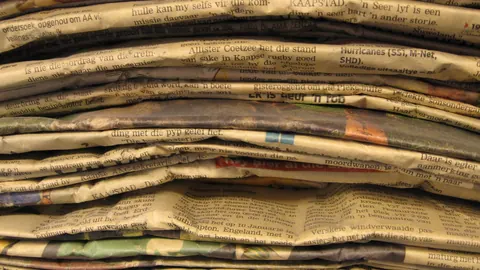 Wysoki stos złożonych starych gazet w bibliotece – pożółkły papier gazetowy widziany z boku, warstwa po warstwie.